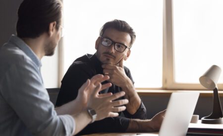 Focused stylish millennial businessman consulting expert, listening to professional advice from boss, coworker, mentor. Business colleagues men meeting, talking at office work table