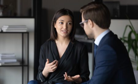 Woman in black shirt talking to a seated man in a blue sweater