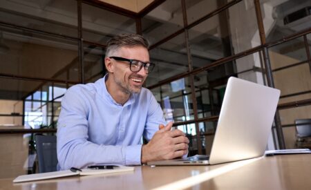 Man wearing blue shirt and glasses smiling and looking at computer
