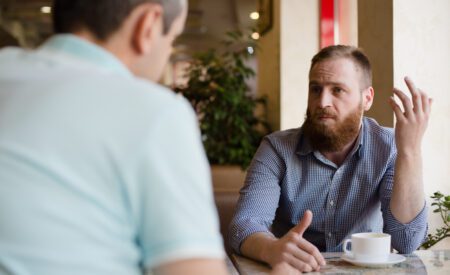Two men talking with coffee mugs in front of them