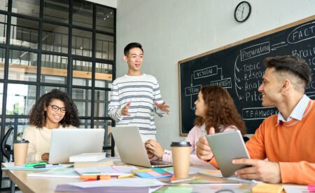 Man standing in front of a chalkboard while talking to colleagues