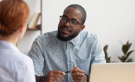 A man in a blue shirt sitting and looking at another person talking